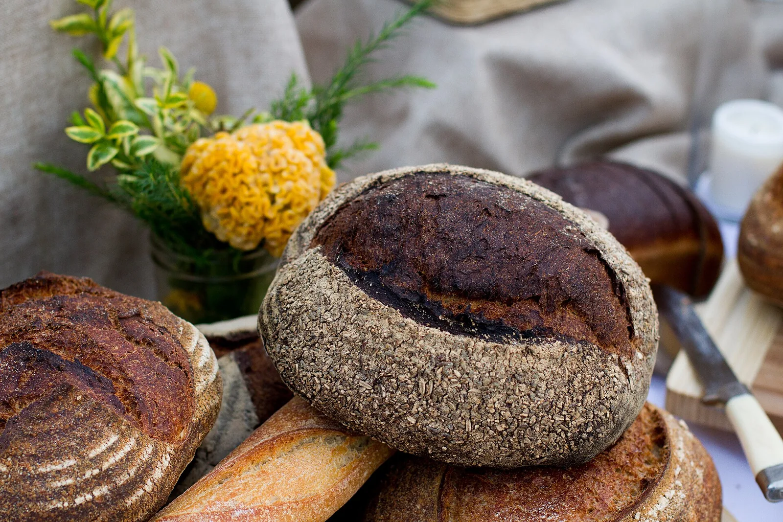 Round loaves of crusty bread beside a jar of yellow flowers