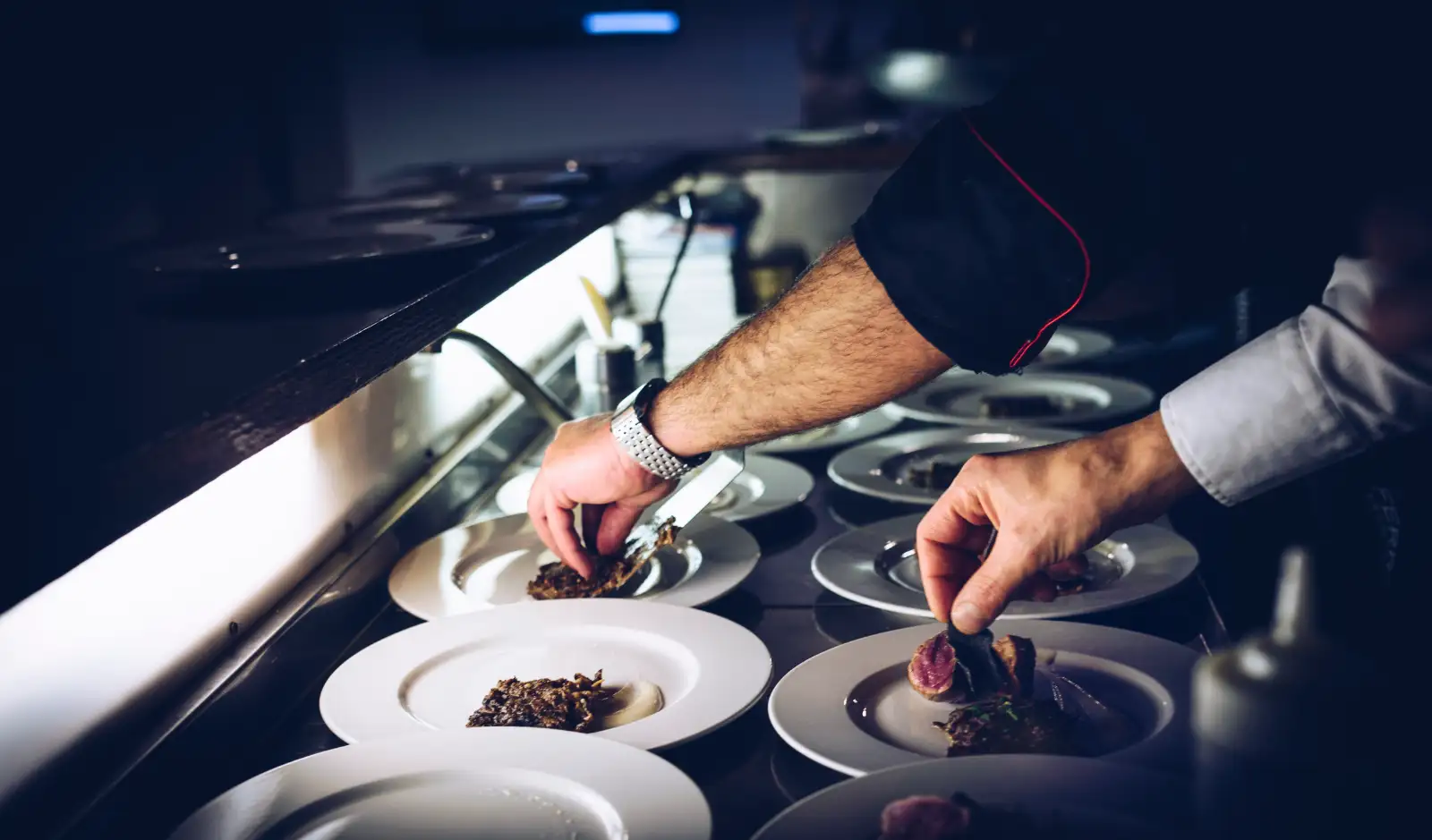 A chef’s hands placing garnish on a row of white plates on a kitchen pass